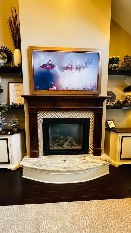 Gold-framed Frame TV in art mode mounted over a tiled fireplace with styled built-ins