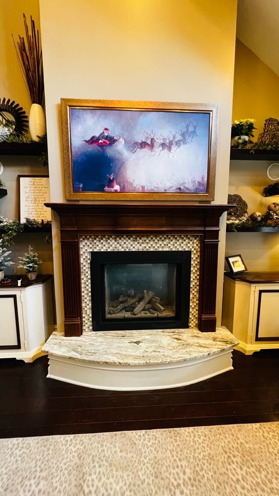 Gold-framed Frame TV in art mode mounted over a tiled fireplace with styled built-ins