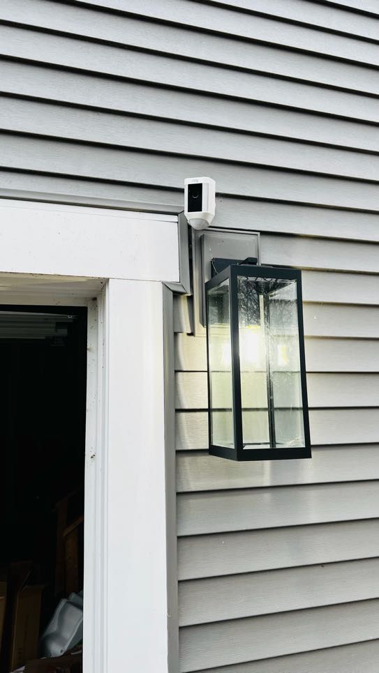 White Ring camera installed beside a black lantern light on grey siding