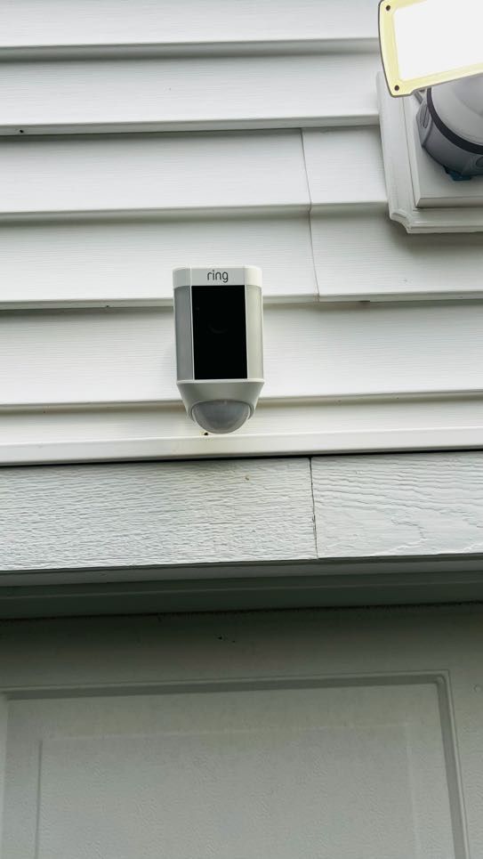 White Ring spotlight camera mounted on white siding next to a floodlight